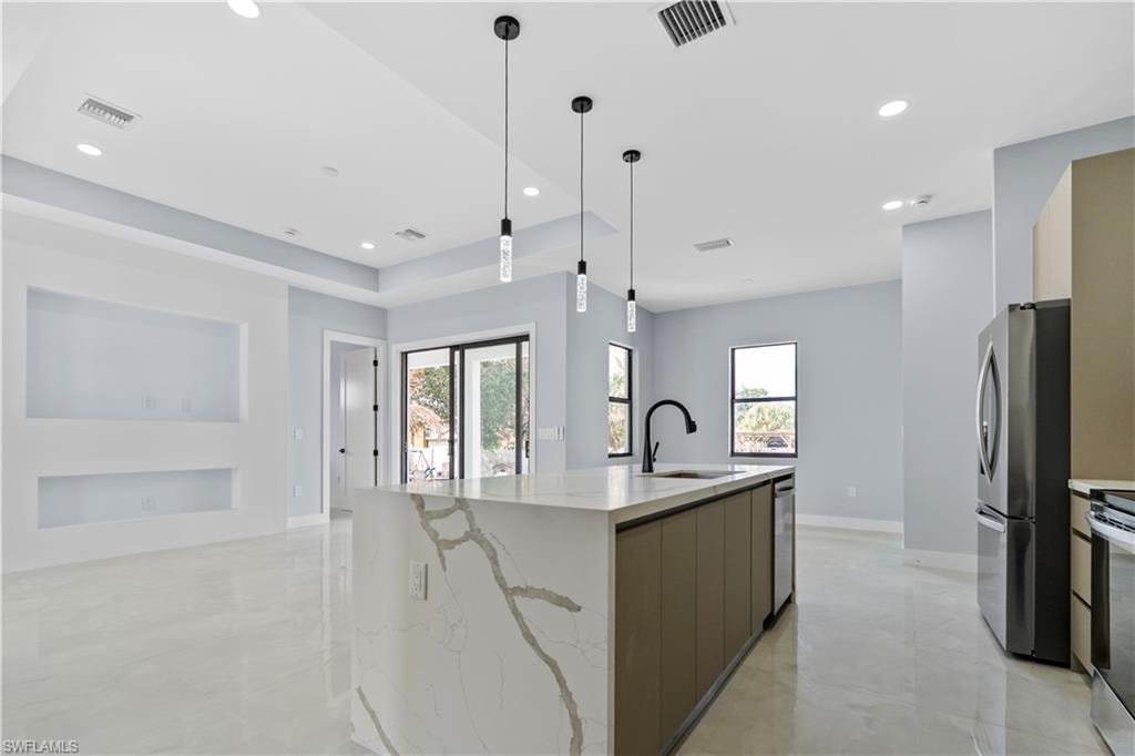 Kitchen featuring light stone counters, an island with sink, stainless steel appliances, and plenty of natural light