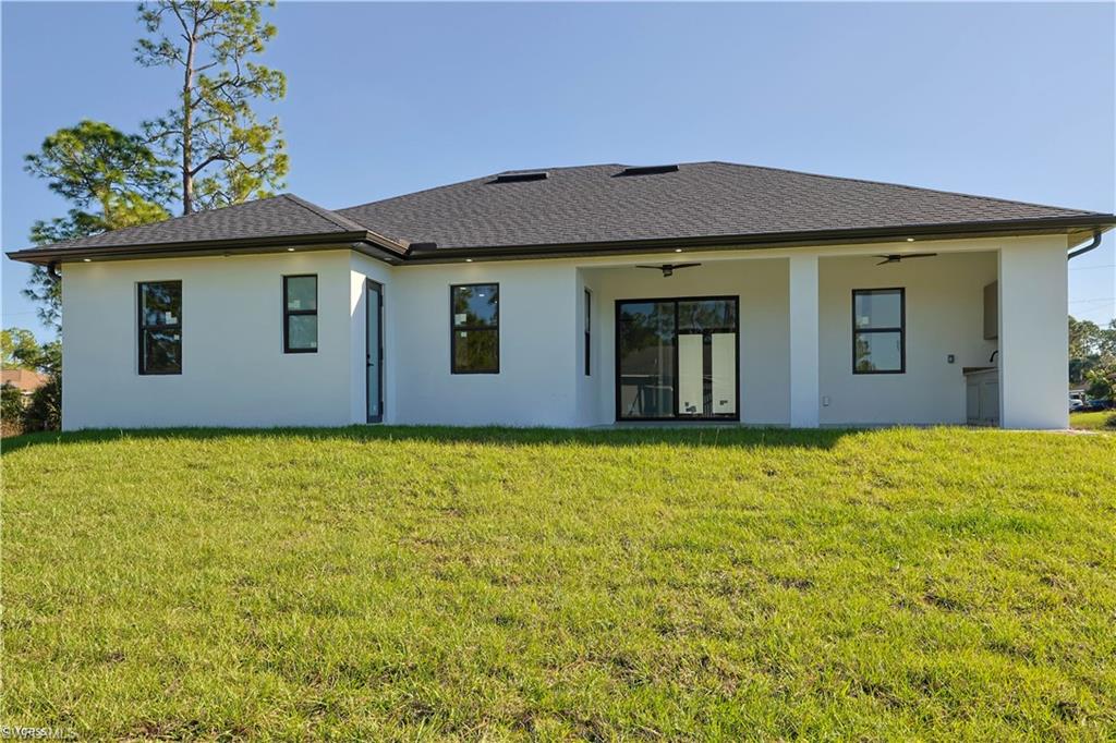 Back of house featuring a ceiling fan, a lawn, stucco siding, a patio, and roof with shingles