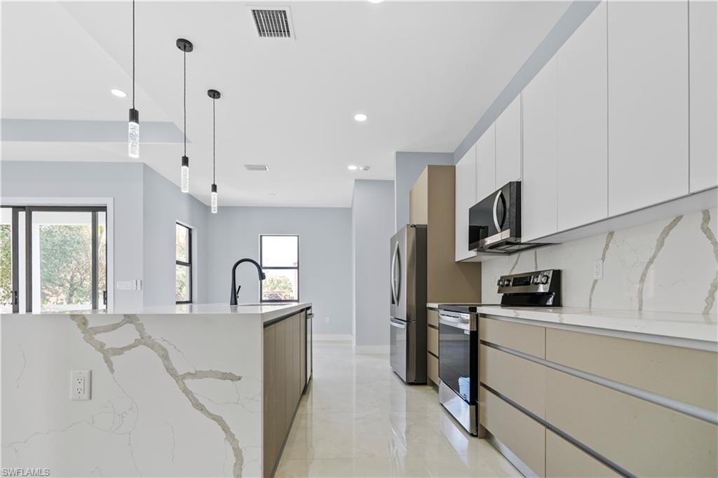 Two tone kitchen featuring stainless steel appliances, two tone cabinetry, light stone countertops, hanging light fixtures, and modern cabinets