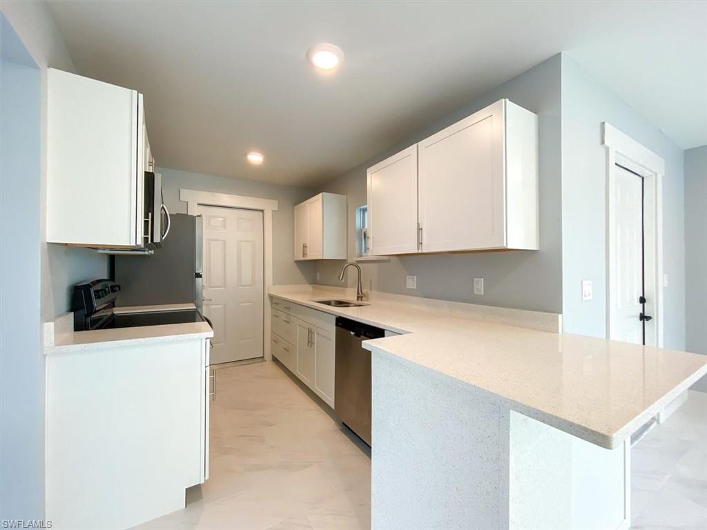 Kitchen featuring white cabinets, light stone counters, a peninsula, appliances with stainless steel finishes, and recessed lighting
