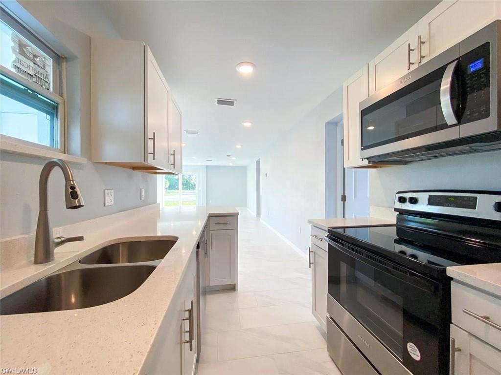 Kitchen with appliances with stainless steel finishes, white cabinets, light stone countertops, and recessed lighting