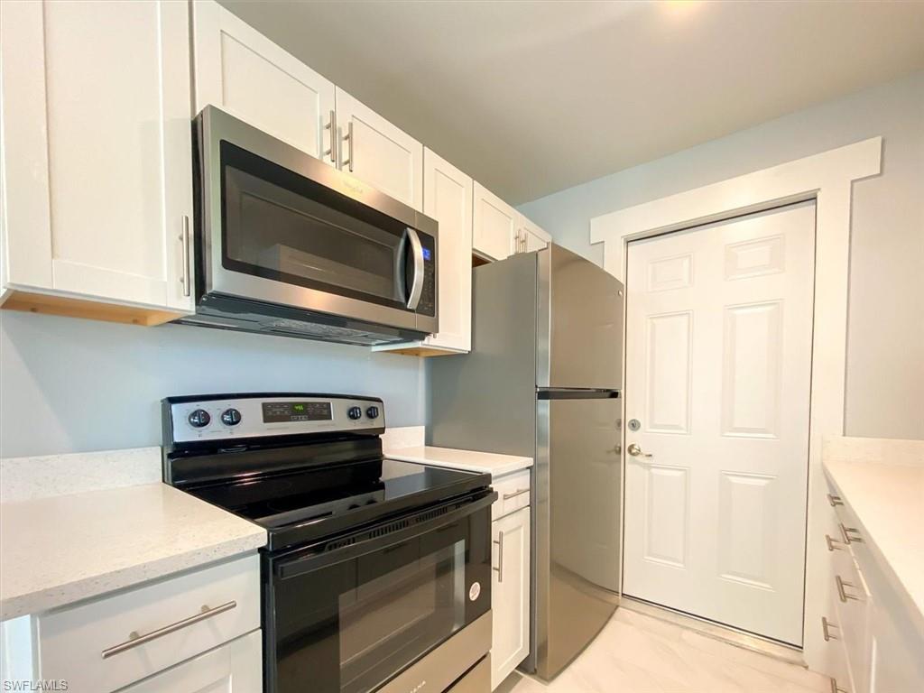 Kitchen with electric stove, stainless steel microwave, white cabinets, and light stone countertops