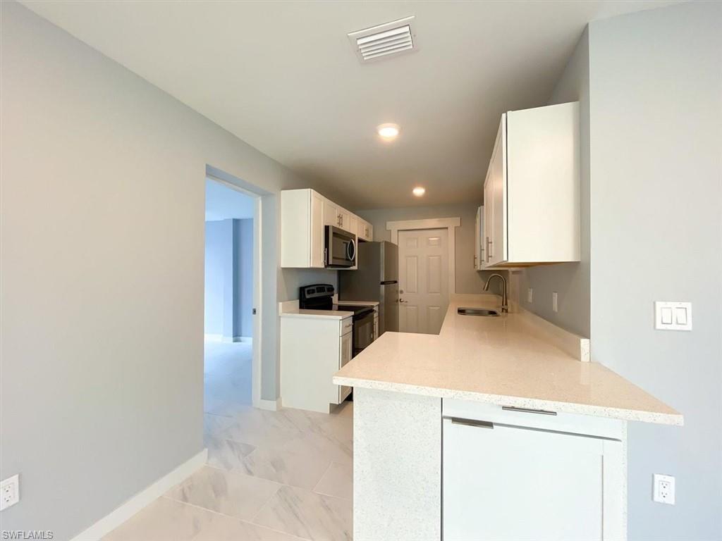 Kitchen with white cabinets, range with electric cooktop, stainless steel microwave, light stone counters, and light marble finish floors