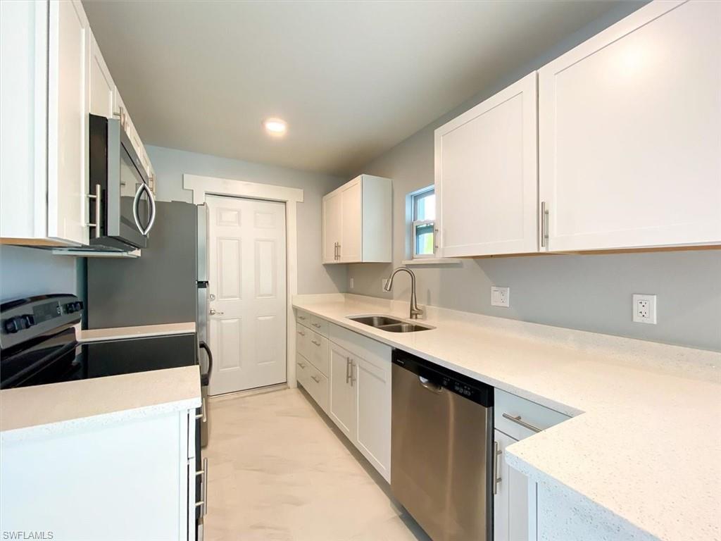 Kitchen with stainless steel appliances, white cabinetry, light stone counters, and light marble finish floors