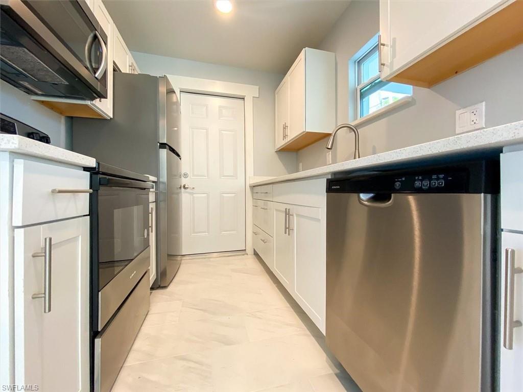 Kitchen featuring stainless steel appliances, white cabinetry, light marble finish floors, and light countertops