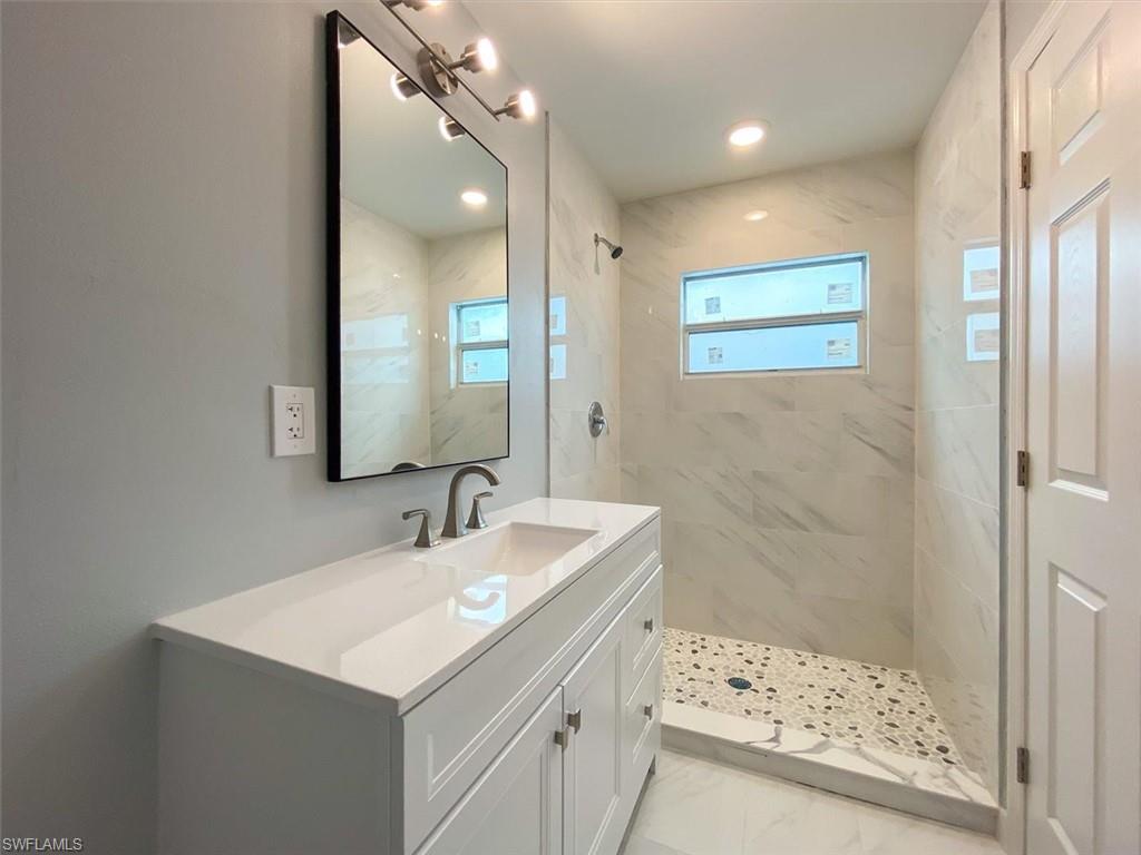 Full bathroom featuring vanity, a marble finish shower, and light marble finish floors