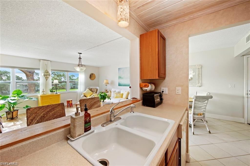 Kitchen with hanging light fixtures, light tile patterned flooring, brown cabinetry, a textured ceiling, and open floor plan