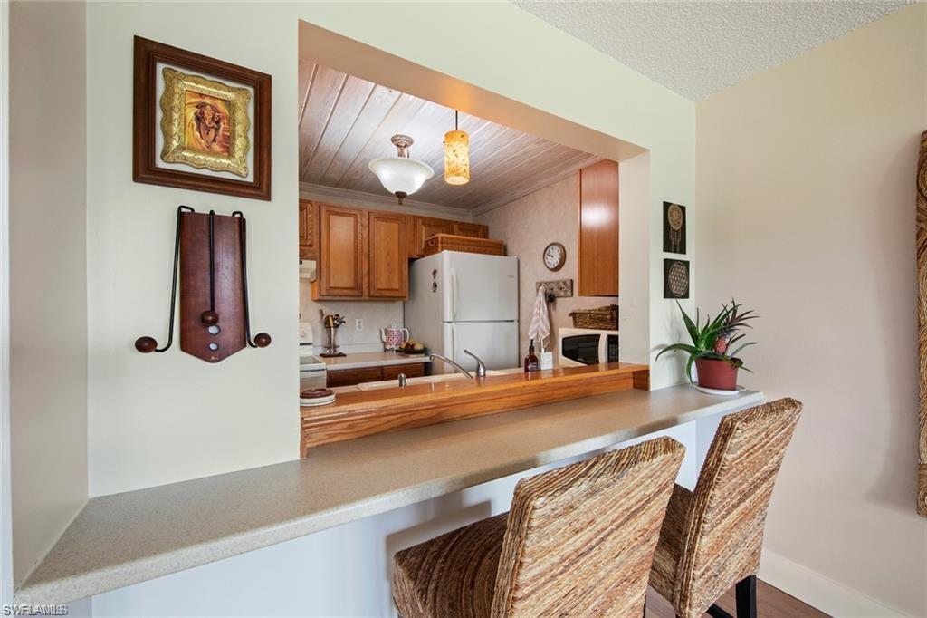 Kitchen with brown cabinetry, light countertops, white appliances, hanging light fixtures, and a kitchen bar
