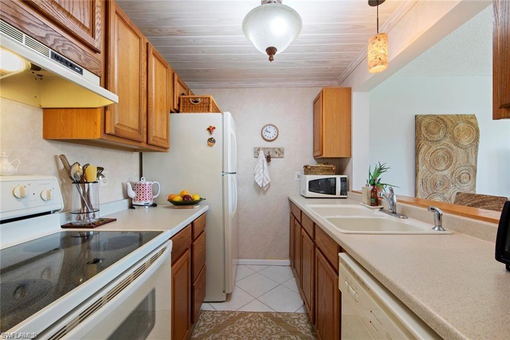 Kitchen featuring white appliances, under cabinet range hood, light countertops, decorative light fixtures, and brown cabinetry
