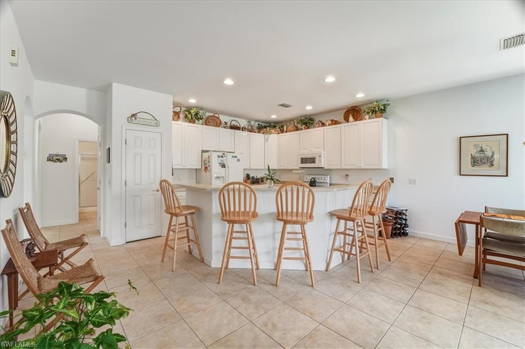 Kitchen with a breakfast bar, arched walkways, white appliances, white cabinets, and light tile patterned flooring
