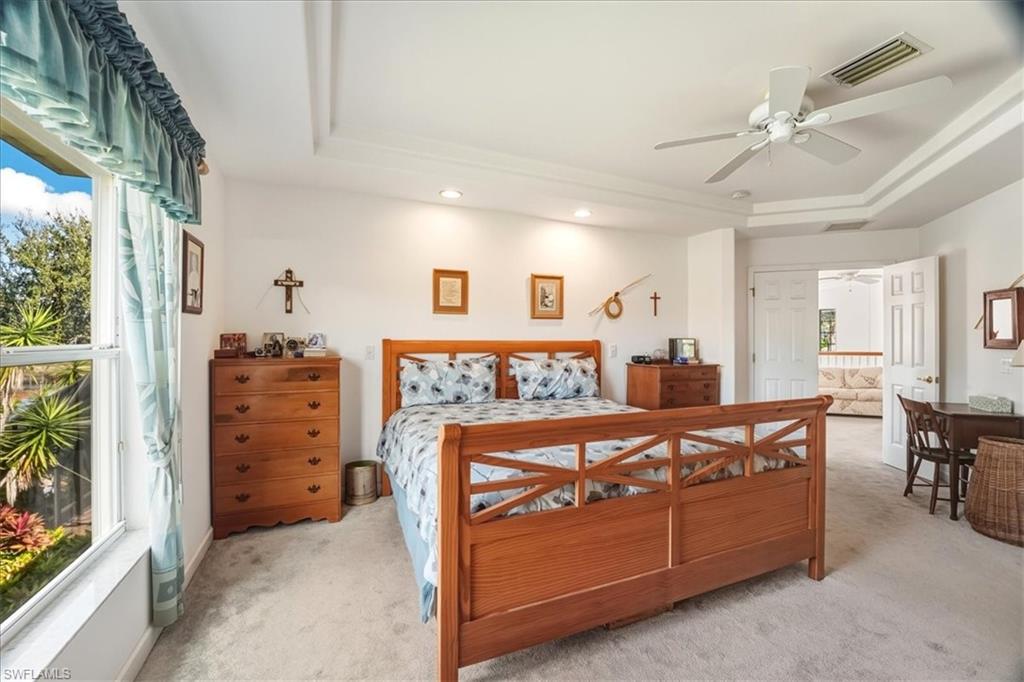 Bedroom with a raised ceiling, light colored carpet, ceiling fan, and recessed lighting