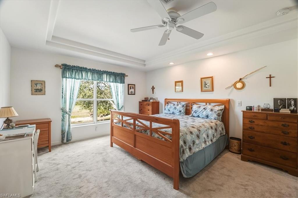 Carpeted bedroom with a tray ceiling and a ceiling fan