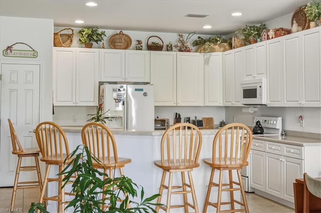 Kitchen featuring white cabinets, white appliances, a breakfast bar, recessed lighting, and light stone countertops