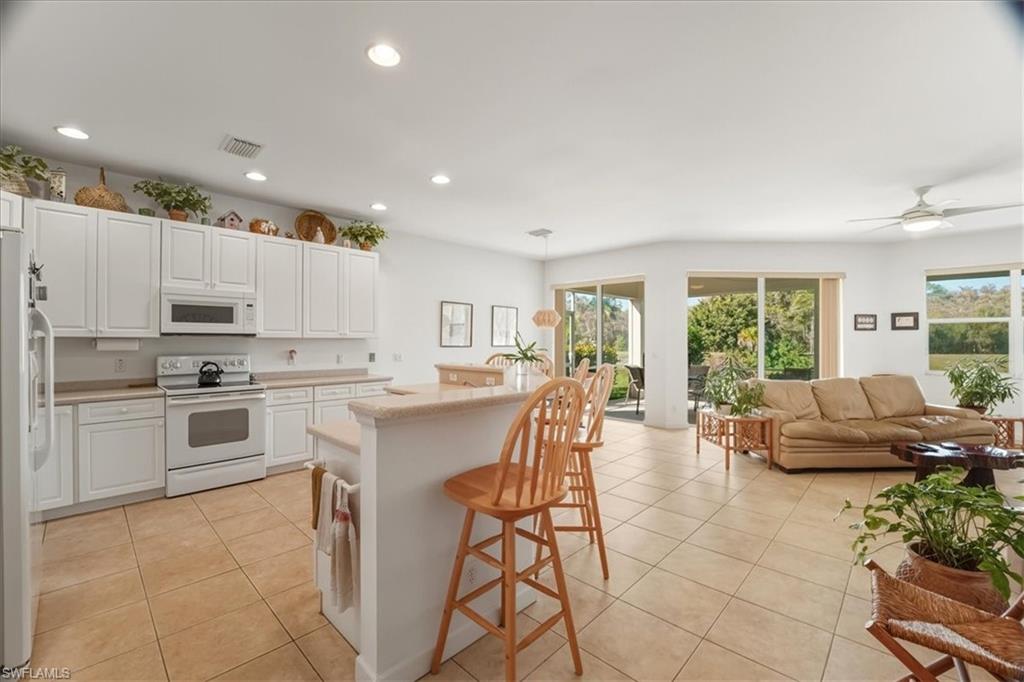 Kitchen featuring white appliances, a breakfast bar area, white cabinetry, recessed lighting, and light tile patterned flooring