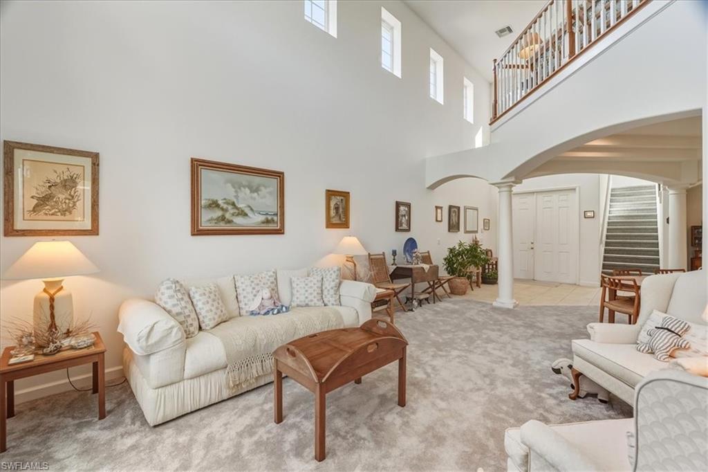 Carpeted living area featuring arched walkways, ornate columns, and a towering ceiling