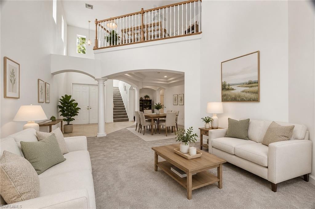 VIRTUALLY STAGED Open-concept living area featuring high ceilings, a second-story interior balcony with white balusters and wood handrail, arched doorways, a carpeted floor, and a double-door entry