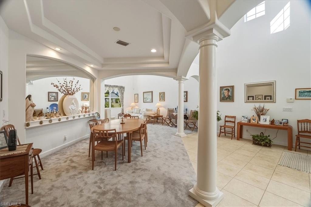 Dining space featuring decorative columns, light carpet, recessed lighting, a raised ceiling, and arched walkways