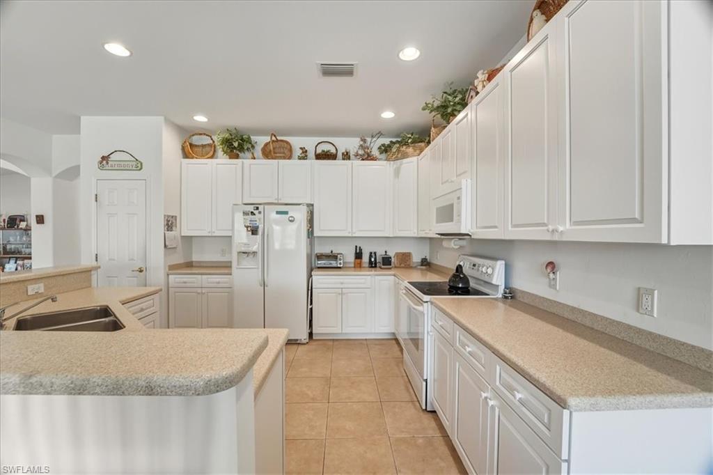 Kitchen with white appliances, recessed lighting, light tile patterned floors, white cabinetry, and a large island