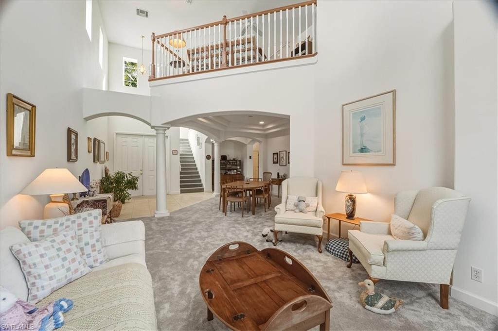 Living room with arched walkways, a towering ceiling, ornate columns, stairway, and carpet floors