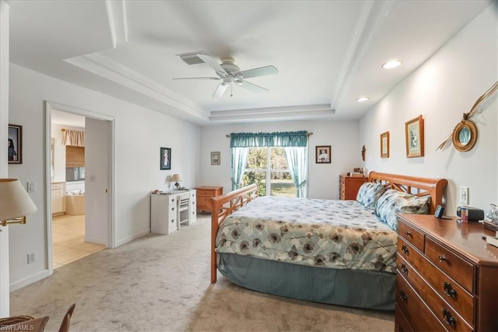 Bedroom with light colored carpet, a raised ceiling, and ceiling fan