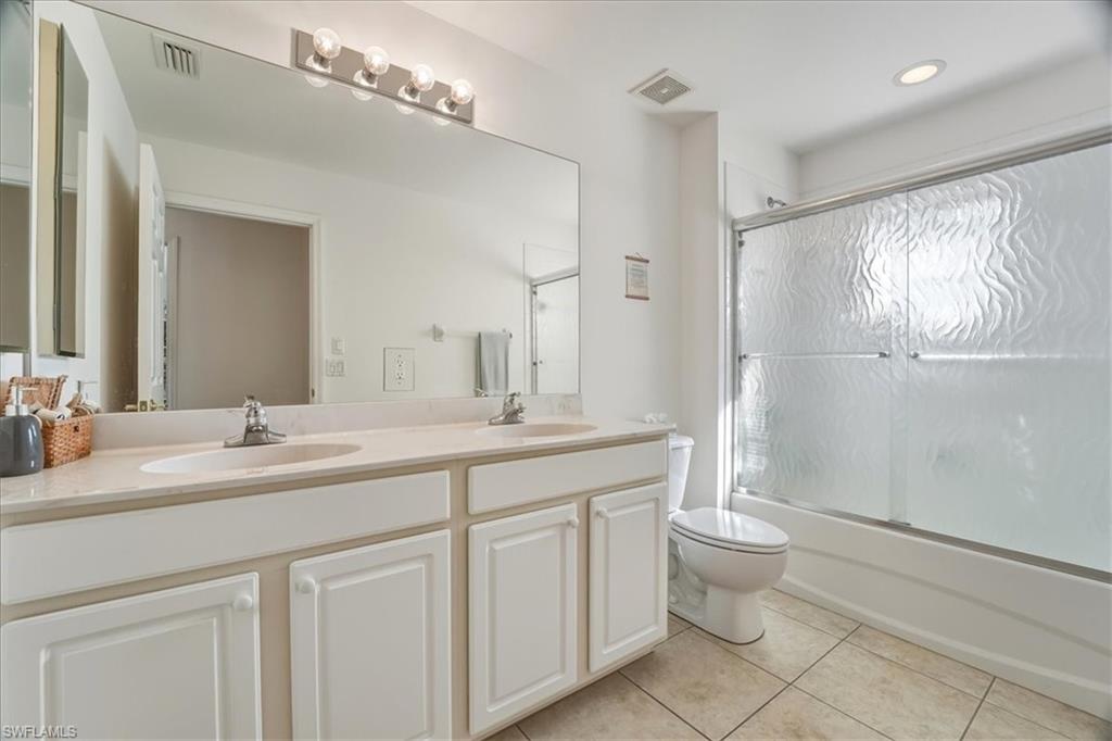 Full bathroom featuring double vanity, light tile patterned floors, and bath / shower combo with glass door