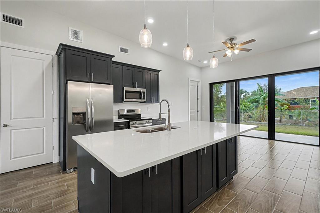 Kitchen featuring dark cabinets, appliances with stainless steel finishes, hanging light fixtures, light stone countertops, and recessed lighting