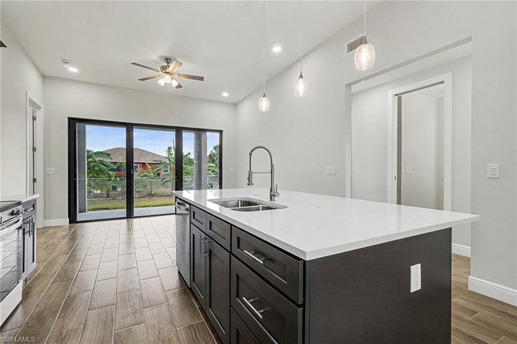 Kitchen with hanging light fixtures, wood finish floors, ceiling fan, a kitchen island with sink, and appliances with stainless steel finishes
