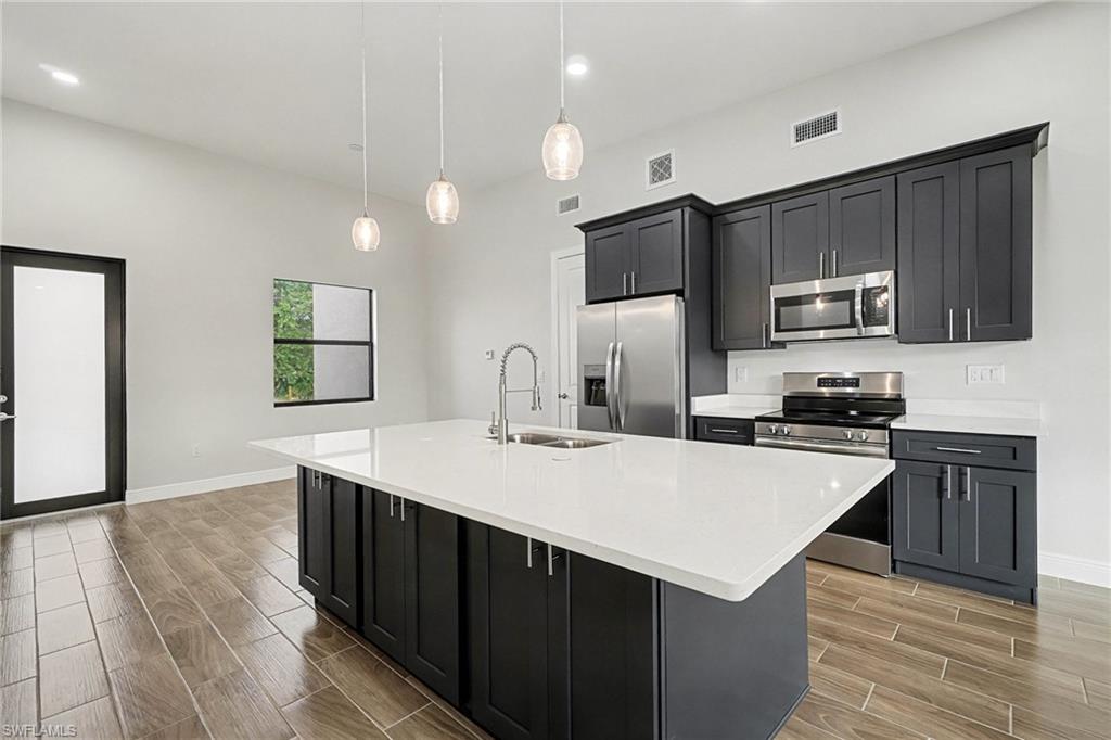 Kitchen with dark cabinetry, wood tiled floors, stainless steel appliances, pendant lighting, and light stone counters
