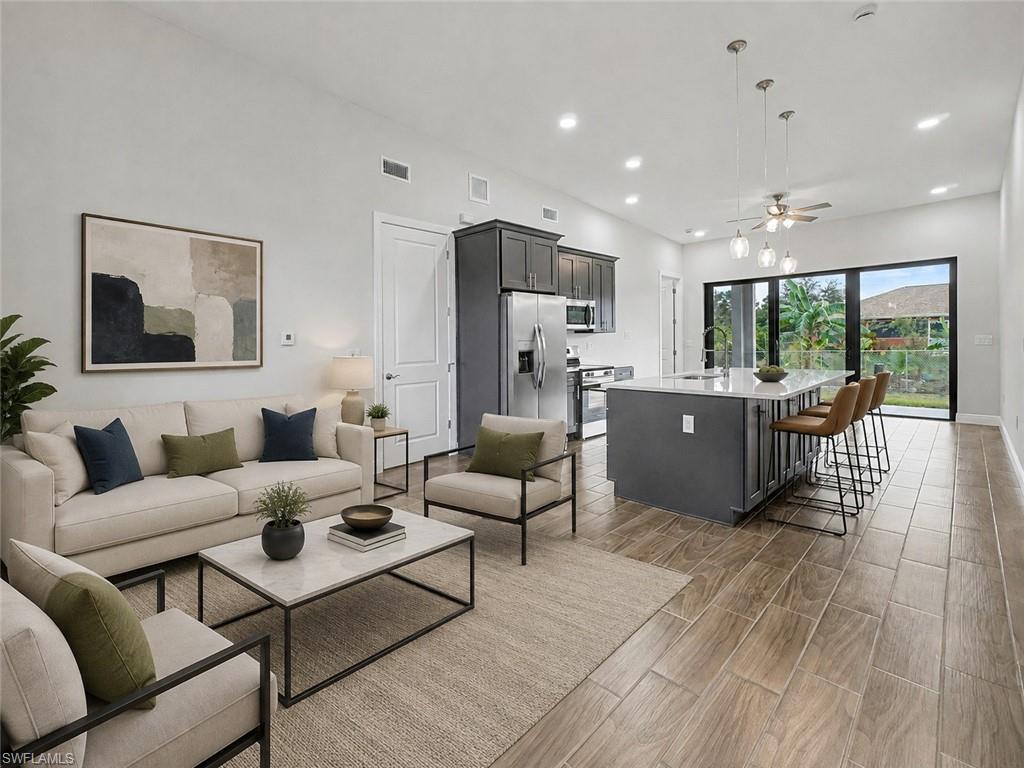 Open-concept living space featuring wood-finish tile flooring, a kitchen island with seating, stainless steel appliances, and dark shaker cabinetry