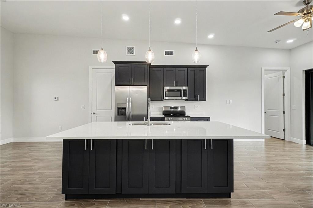 Kitchen with dark cabinetry, stainless steel appliances, an island with sink, light stone countertops, and a kitchen bar