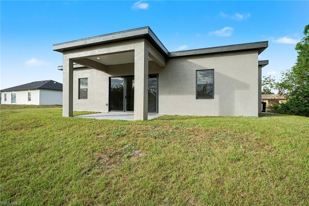 Rear view of house with a patio area, stucco siding, and a yard