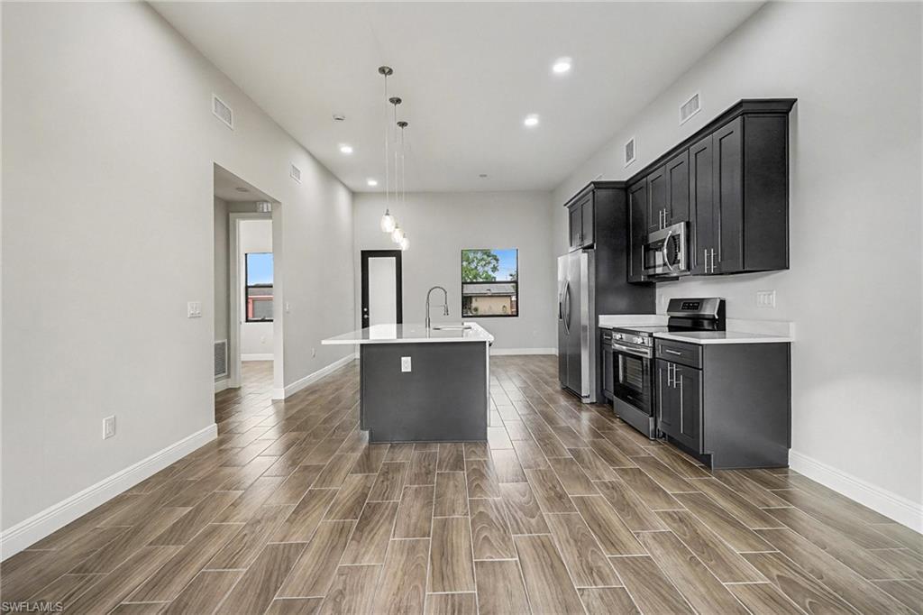 Kitchen featuring an island with sink, stainless steel appliances, dark cabinets, decorative light fixtures, and recessed lighting