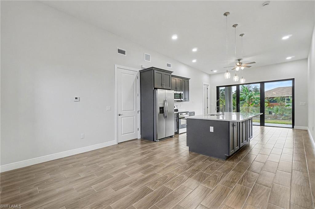 Kitchen with hanging light fixtures, a kitchen island with sink, ceiling fan, light stone counters, and wood finish floors