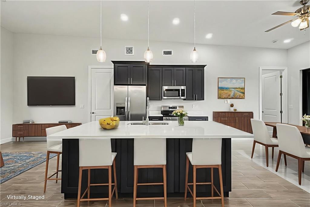 Kitchen featuring dark cabinetry, a kitchen breakfast bar, stainless steel appliances, an island with sink, and light stone countertops