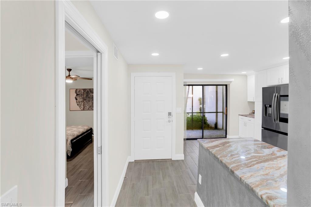 Kitchen featuring white cabinetry, stainless steel fridge, wood tiled floors, light stone countertops, and recessed lighting