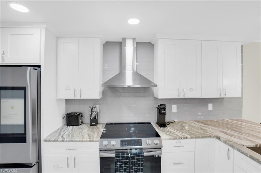 Kitchen featuring appliances with stainless steel finishes, wall chimney exhaust hood, light stone counters, white cabinets, and recessed lighting