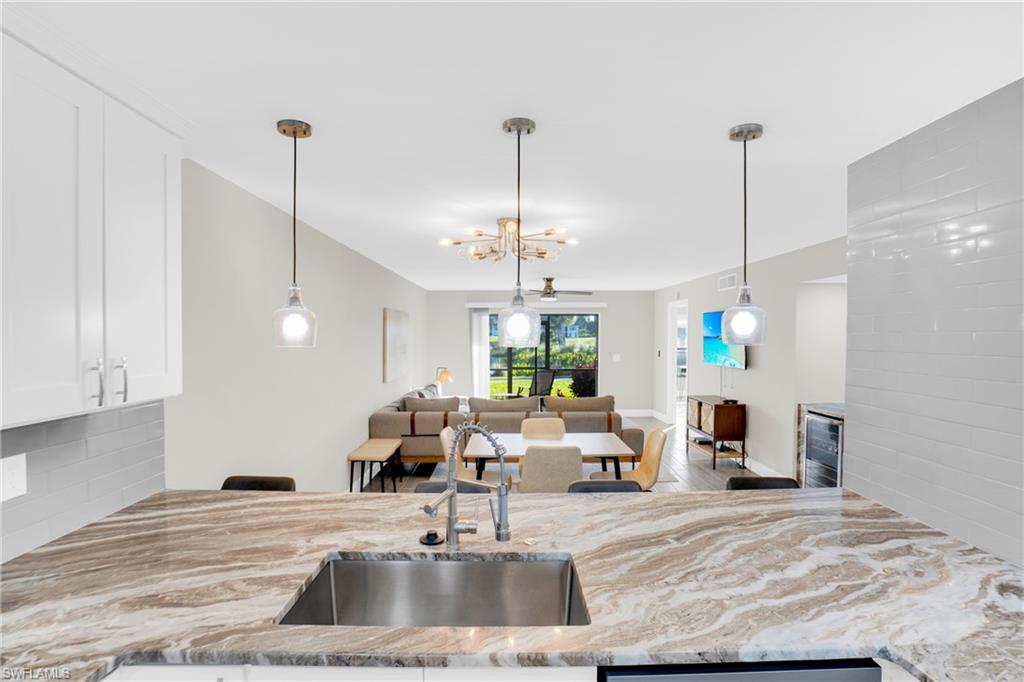 Kitchen featuring decorative light fixtures, light stone countertops, white cabinetry, a chandelier, and backsplash