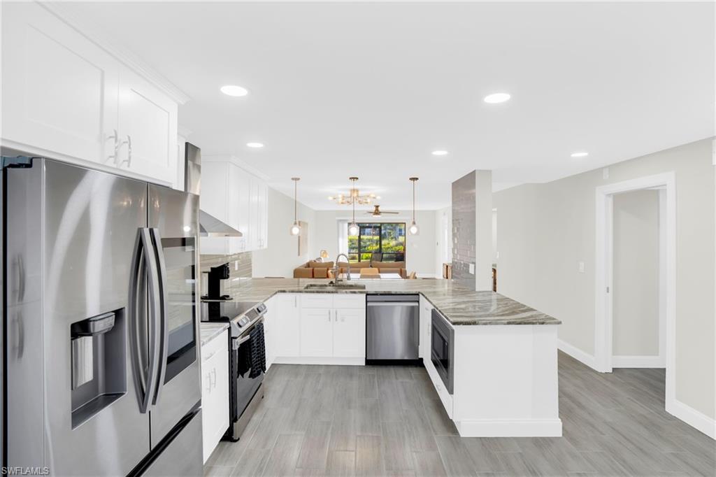 Kitchen with stainless steel appliances, white cabinets, a peninsula, decorative light fixtures, and a chandelier