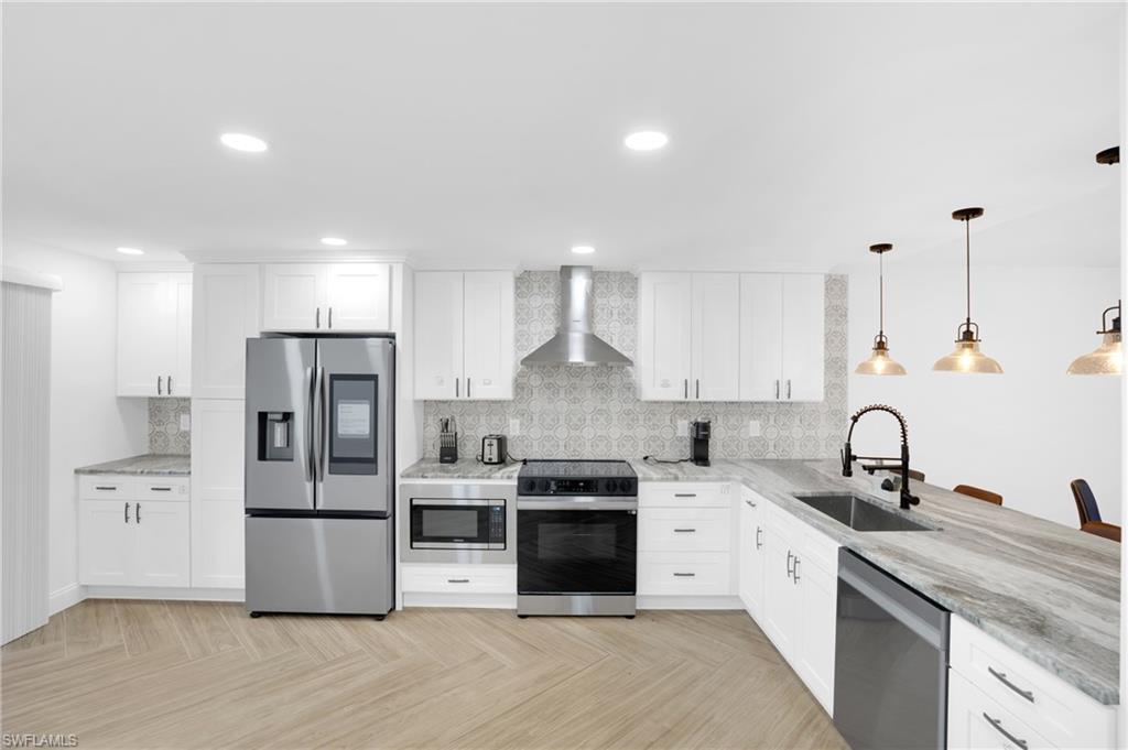 Kitchen featuring stainless steel appliances, white cabinets, wall chimney range hood, pendant lighting, and recessed lighting