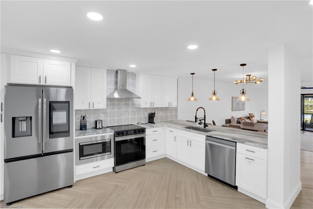 Kitchen with stainless steel appliances, wall chimney range hood, white cabinets, decorative backsplash, and recessed lighting
