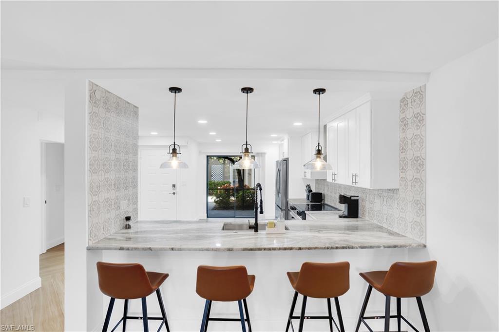 Kitchen featuring white cabinetry, a kitchen bar, tasteful backsplash, pendant lighting, and light stone counters