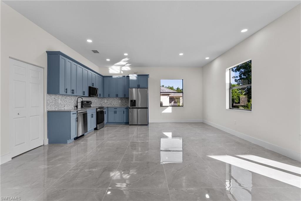 Kitchen featuring appliances with stainless steel finishes, light countertops, light marble finish floors, blue cabinets, and decorative backsplash