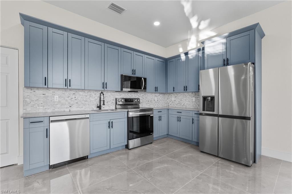Kitchen with appliances with stainless steel finishes, tasteful backsplash, light stone countertops, and light marble finish floors