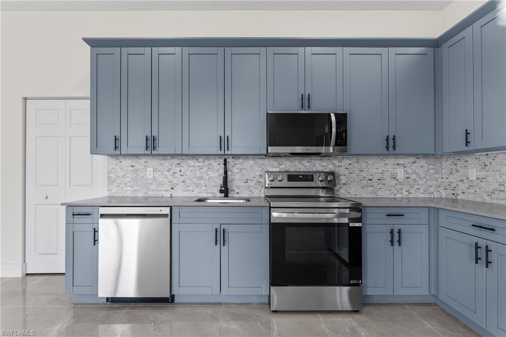 Kitchen with appliances with stainless steel finishes, light stone counters, and decorative backsplash
