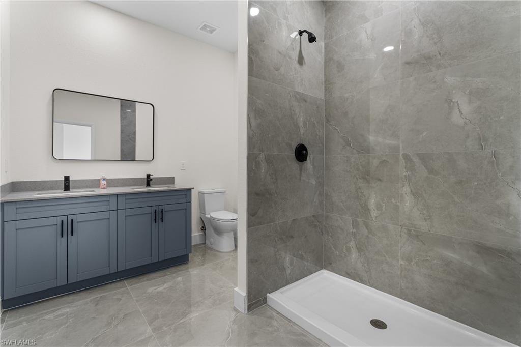 Full bath with double vanity, a tile shower, and light marble finish flooring