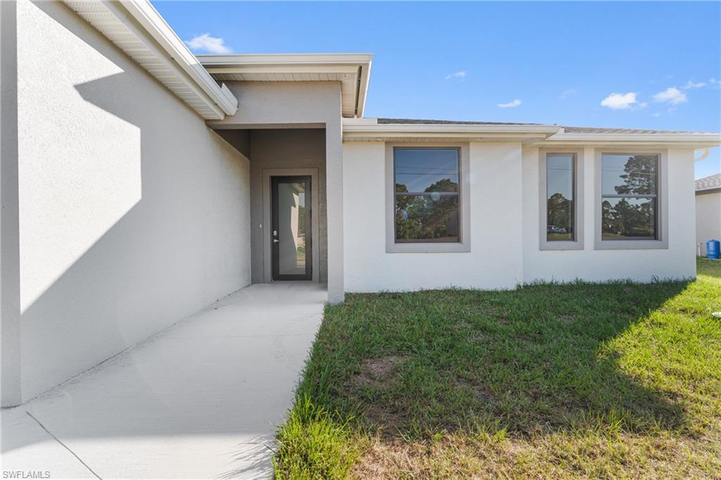 Entrance to property with stucco siding and a lawn