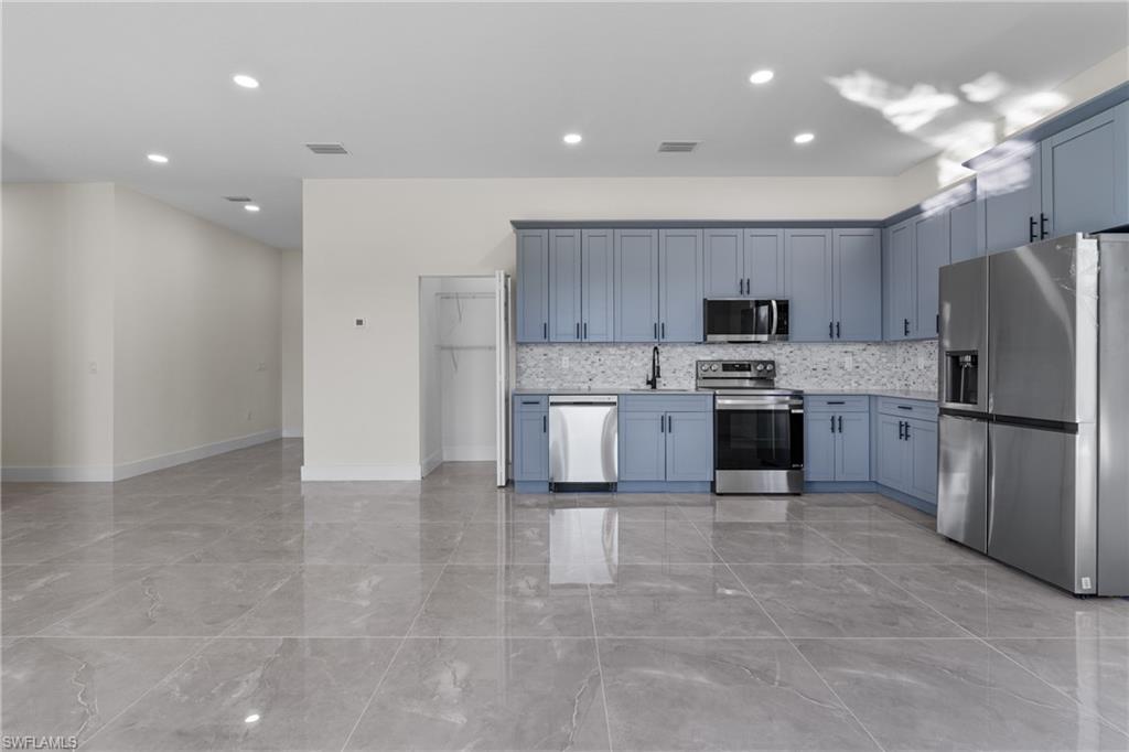 Kitchen with appliances with stainless steel finishes, recessed lighting, light marble finish flooring, tasteful backsplash, and open floor plan