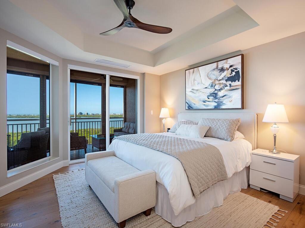 Bedroom featuring a water view, a tray ceiling, access to exterior, ceiling fan, and wood-type flooring