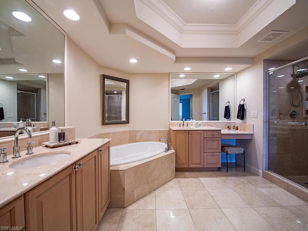 Bathroom with a raised ceiling, a stall shower, a garden tub, two vanities, and crown molding