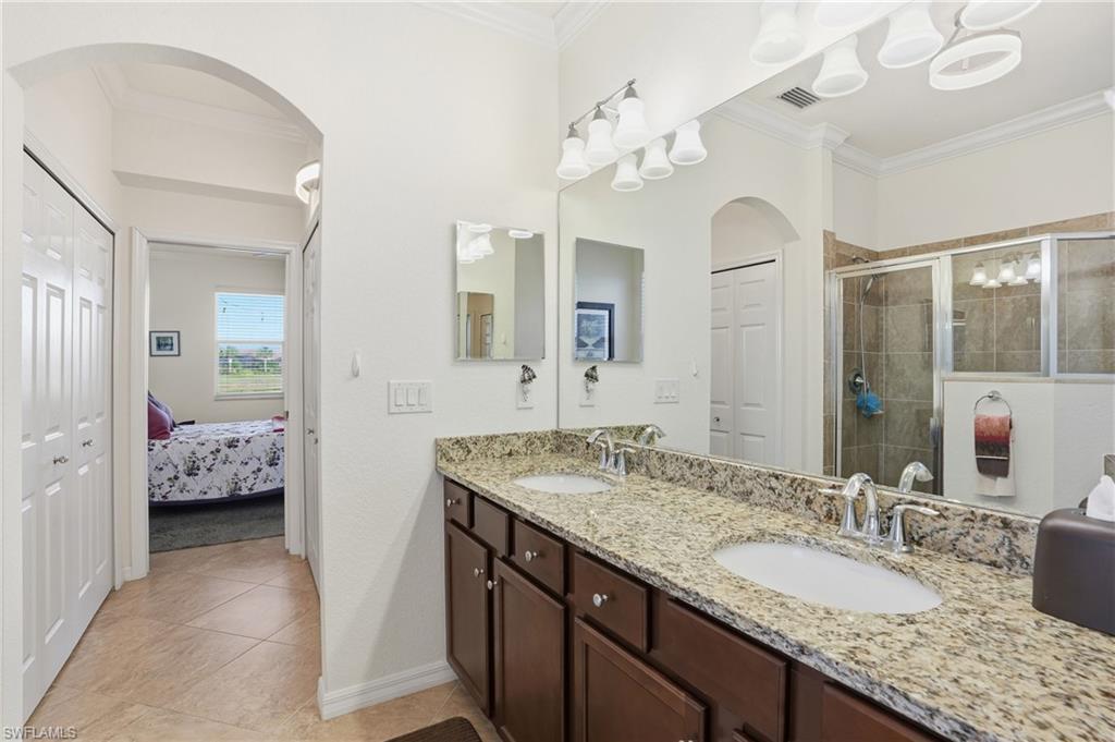 Bathroom featuring double vanity, ornamental molding, a stall shower, a closet, and light tile patterned floors